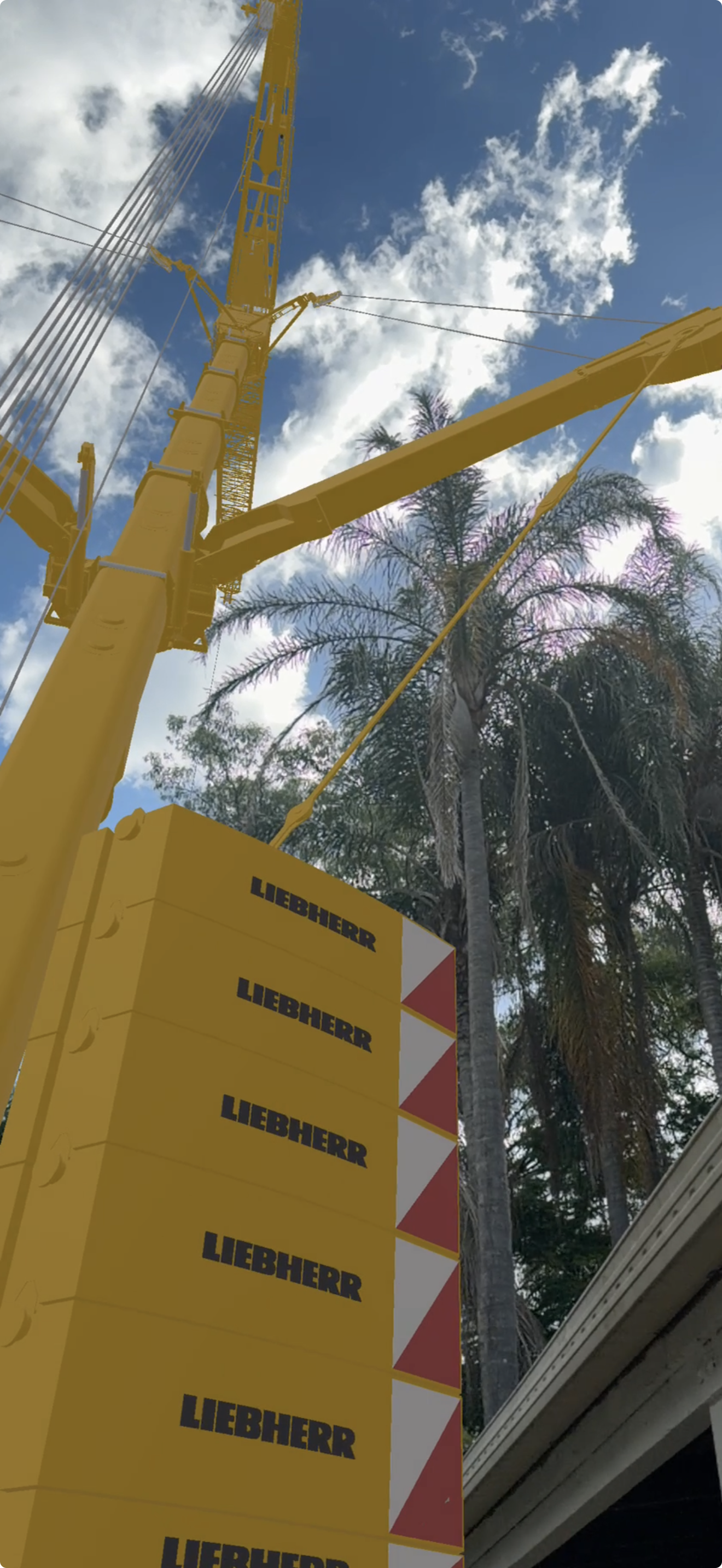 VisualQuip augmented reality view looking up at a yellow Liebherr crane, boom and counterweights against a blue sky